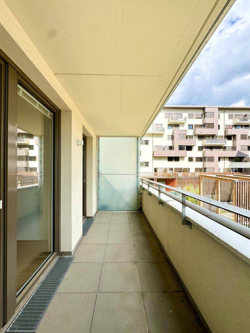 Langer Balkon mit Fliesenboden und Blick auf die umliegenden Gebäude der Wohnanlage.