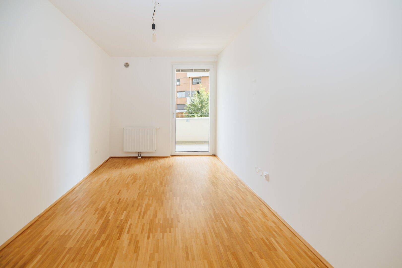 Helles Zimmer mit Parkettboden und Zugang zu einem kleinen Balkon, ideal für ein Schlafzimmer.