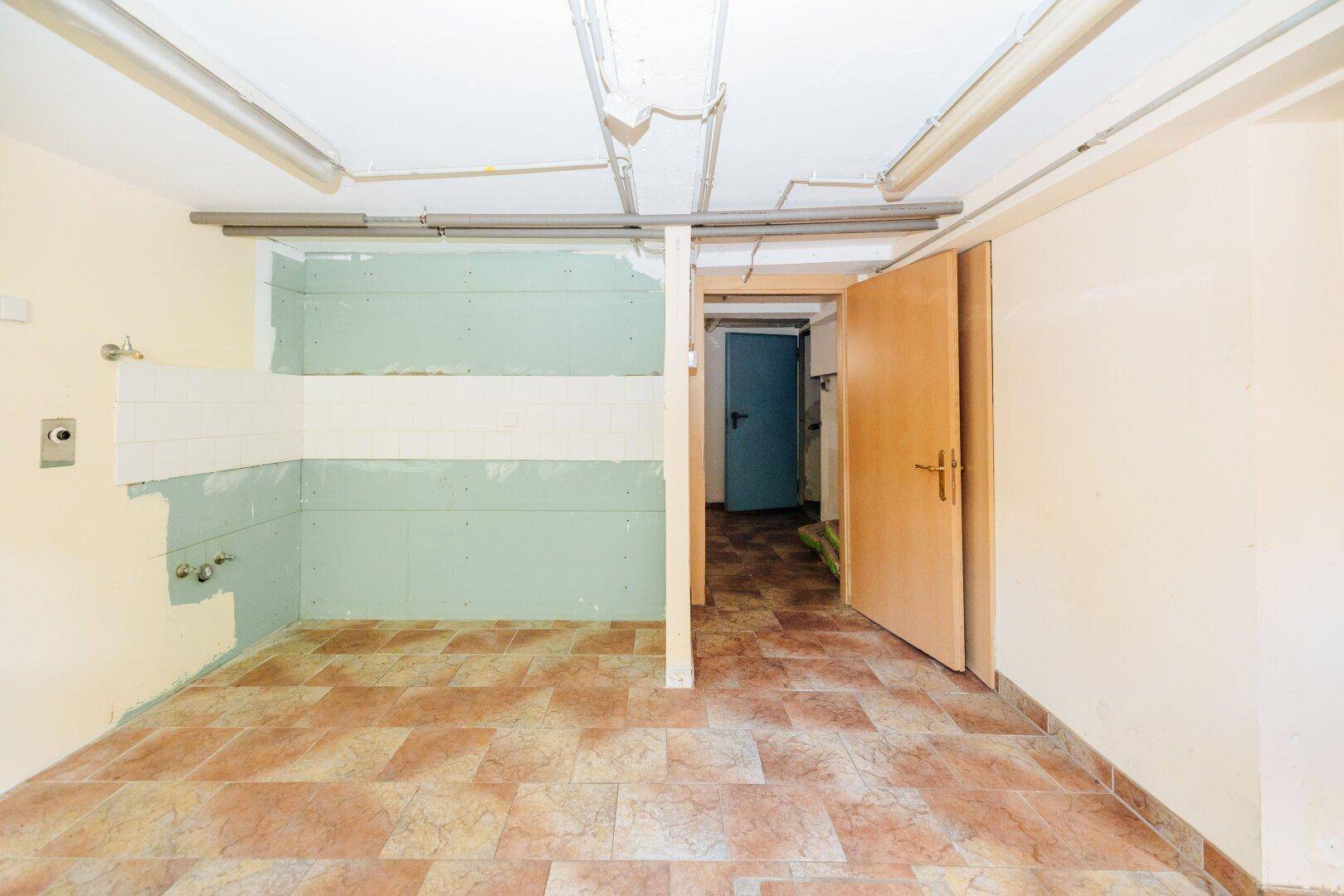 Kellerraum in Renovierung mit Fliesenboden und sichtbaren Installationen.