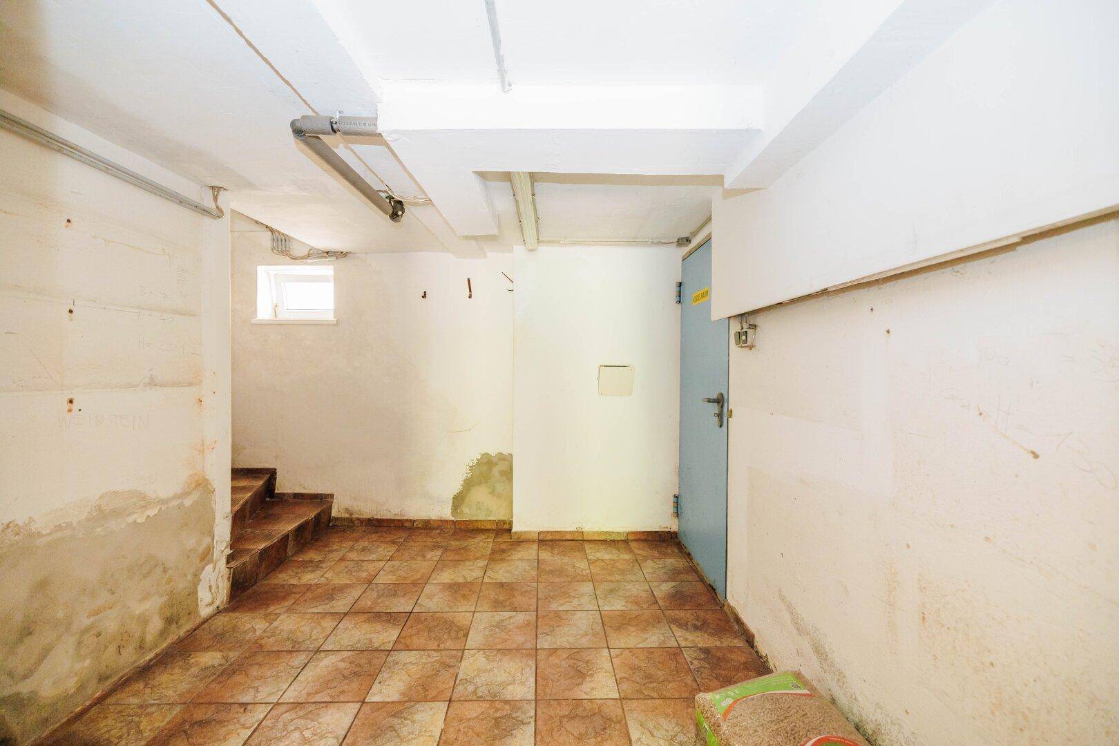 Kellerflur mit Fliesenboden, Treppe und Zugang zu weiteren Räumen.