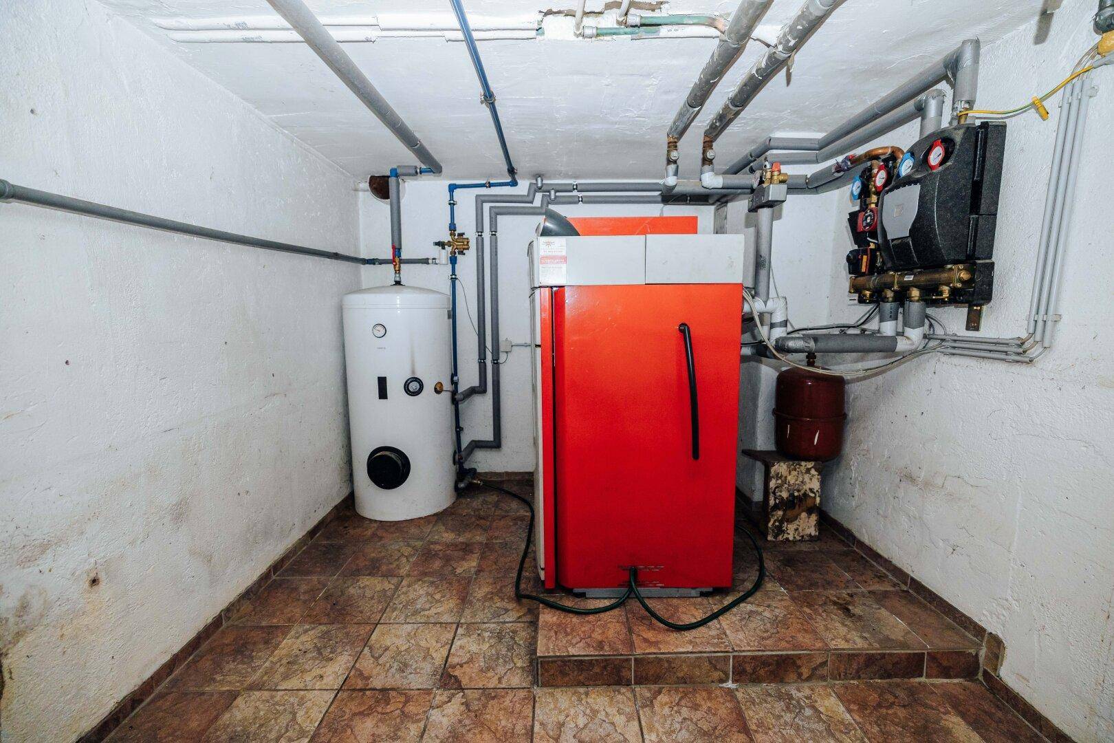 Heizungsraum im Keller mit moderner Heizungsanlage und Warmwasserspeicher.