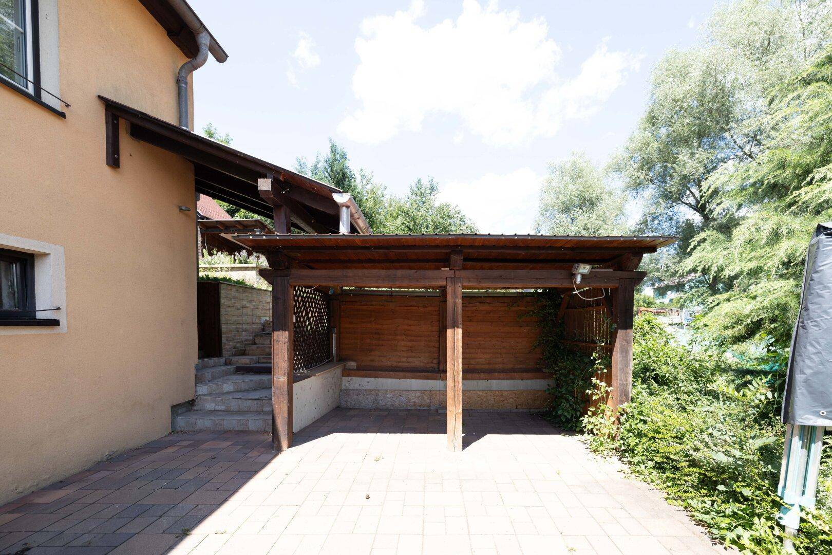 Geräumige gepflasterte Terrasse mit Holzüberdachung und Zugang zum Gartenbereich.