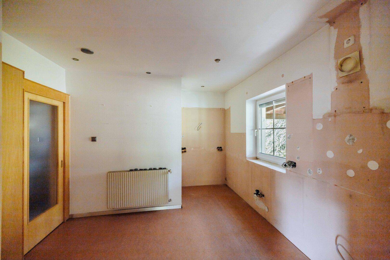 Unfertige Küche mit Fenster, Heizkörper und vorbereiteten Anschlüssen für die Küchenzeile.