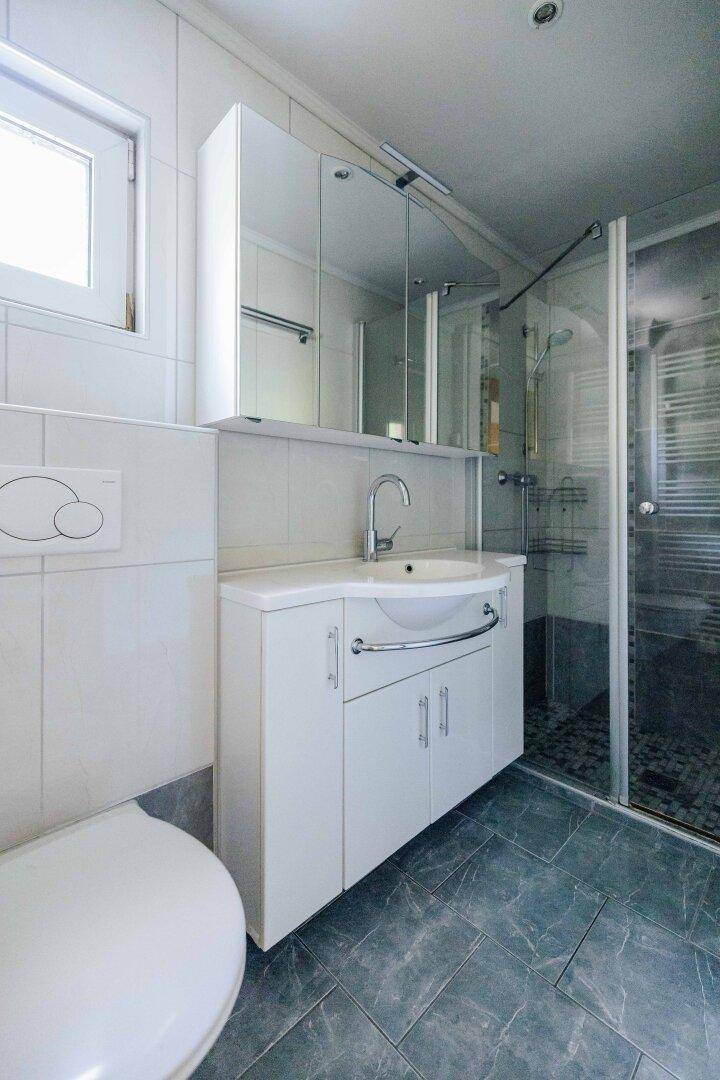 Modernes Badezimmer mit Duschkabine, Waschtisch und wandhängendem WC in hellen Fliesen.