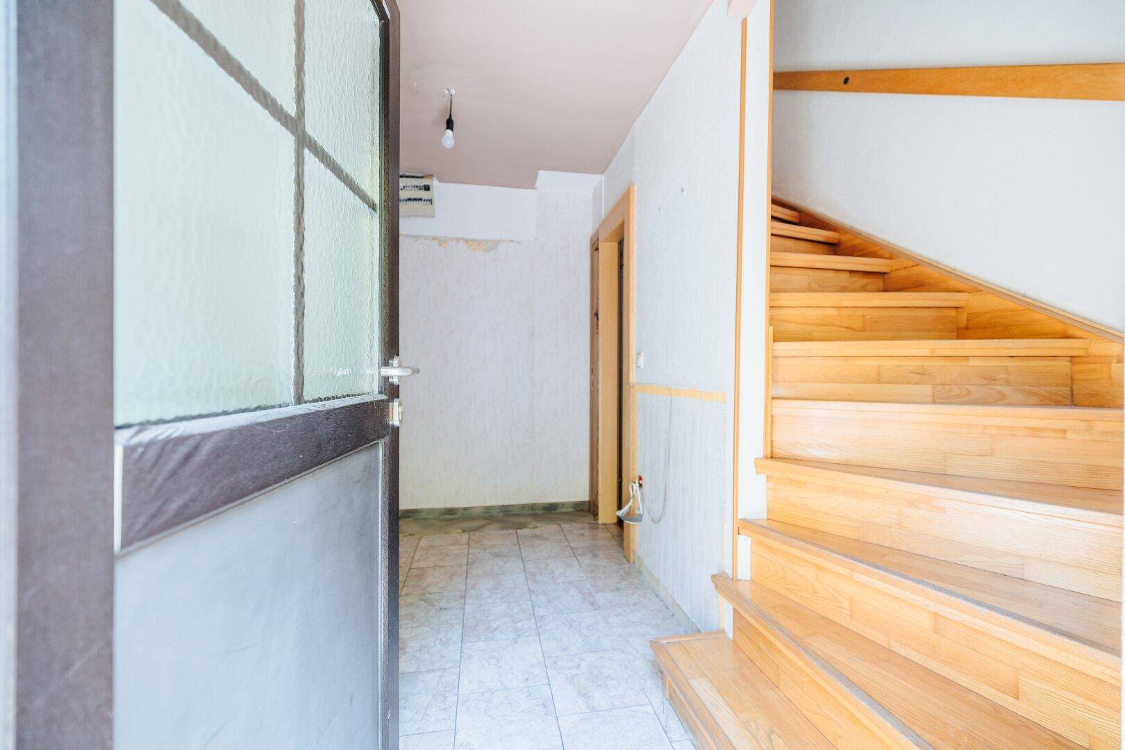 Heller Flur mit gefliestem Boden und Holztreppe zum Obergeschoss.