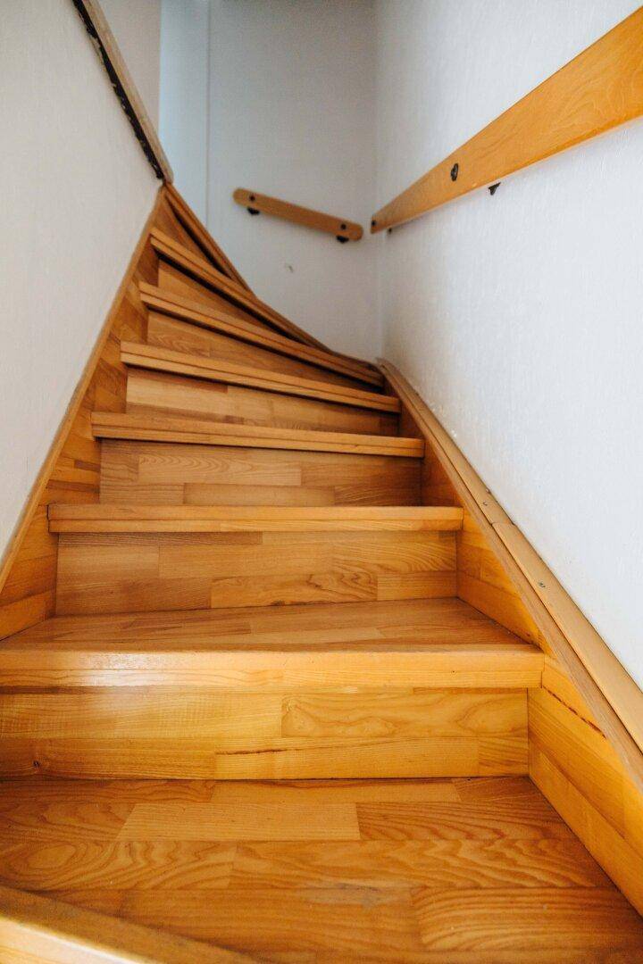 Holztreppe mit hellem Holz und schlichtem Geländer, die in ein Obergeschoss führt.