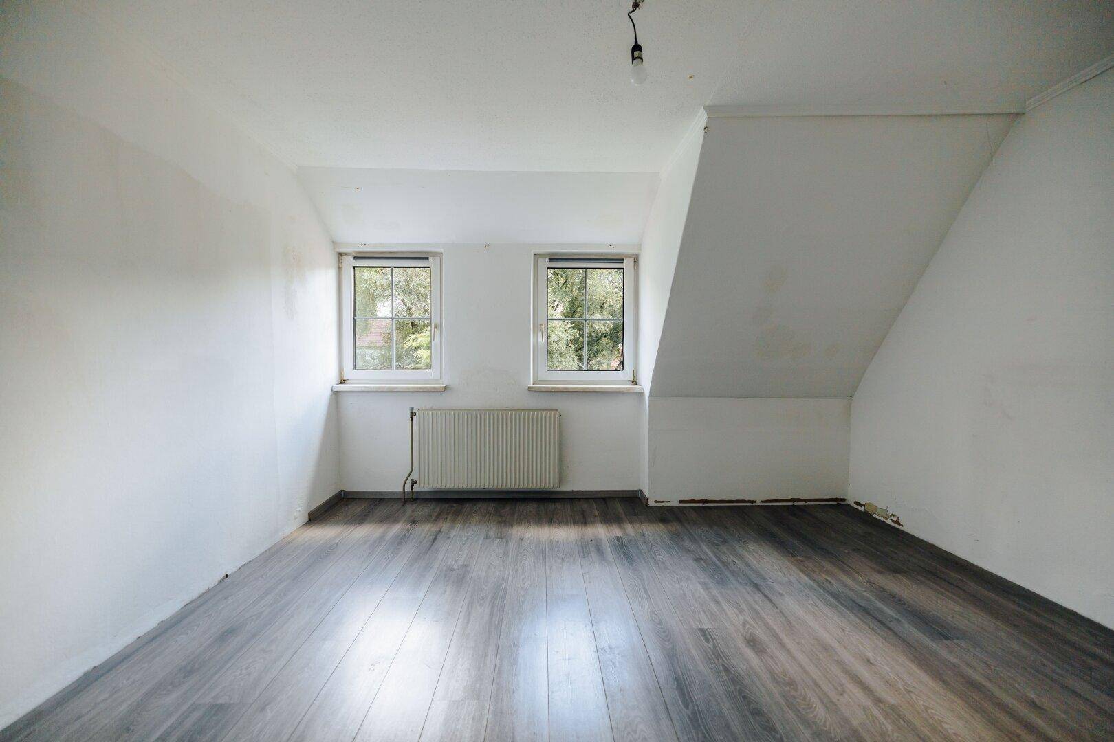 Helles Schlafzimmer mit Laminatboden, zwei Fenstern und Dachschräge.
