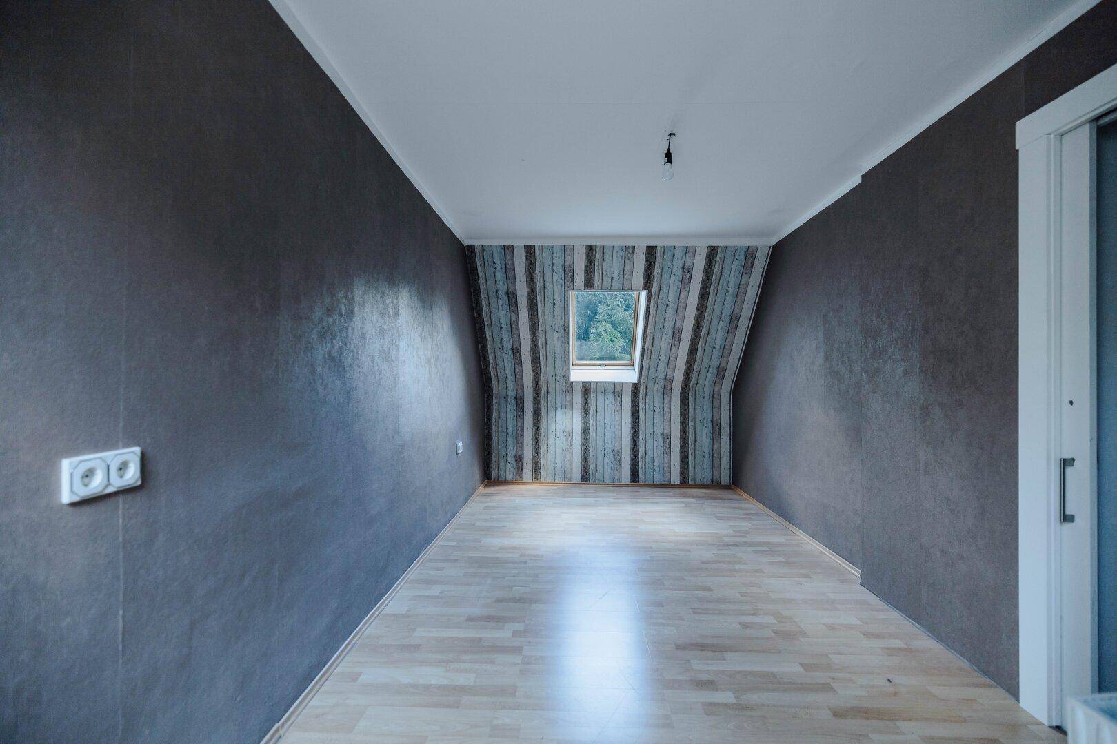 Langes Zimmer mit Laminatboden, Dachfenster und dunkler Wandgestaltung.