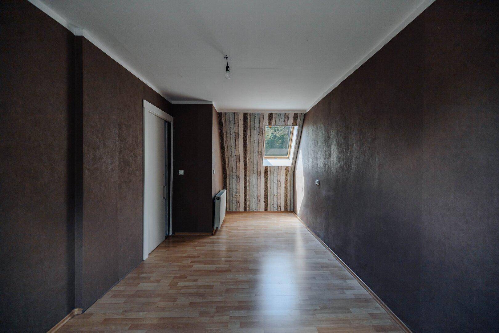 Geräumiges Zimmer mit Laminatboden, Dachfenster und dunklen Wänden.