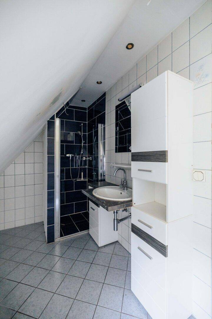 Badezimmer im Dachgeschoss mit Dusche, Waschtisch und schrägen Wänden.
