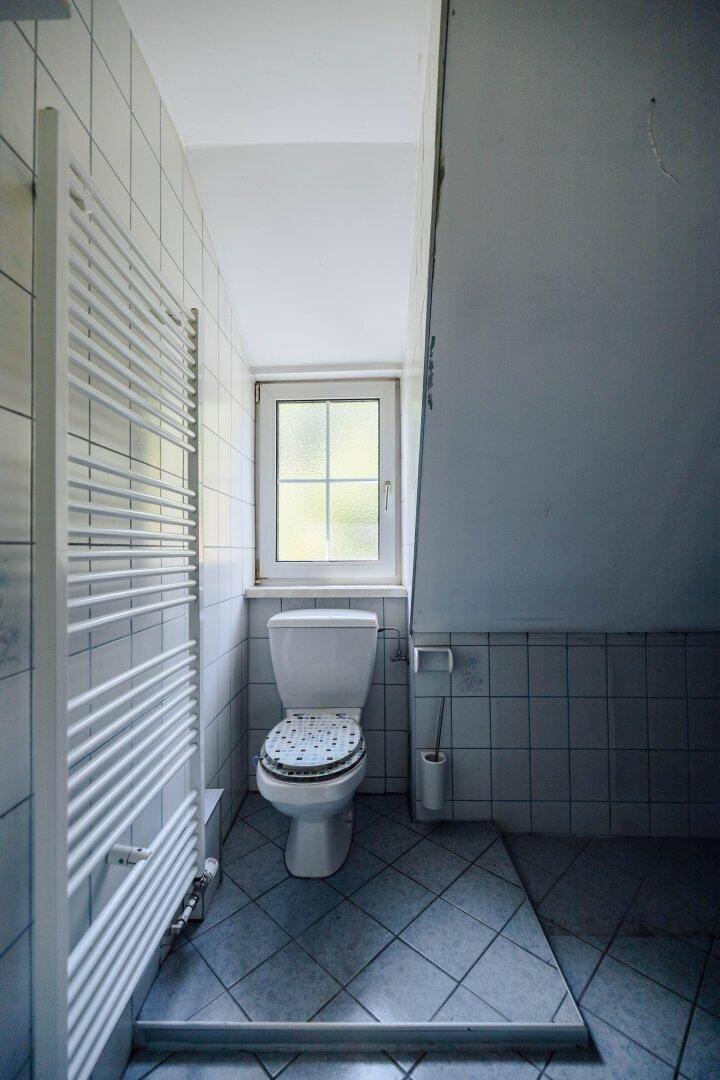 WC-Bereich mit Fenster, Heizkörper und weißen Fliesen im Badezimmer.
