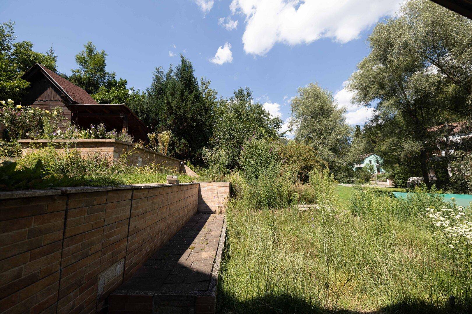 Terrassierter Gartenbereich mit Ziegelmauer und Blick auf die grüne Landschaft.