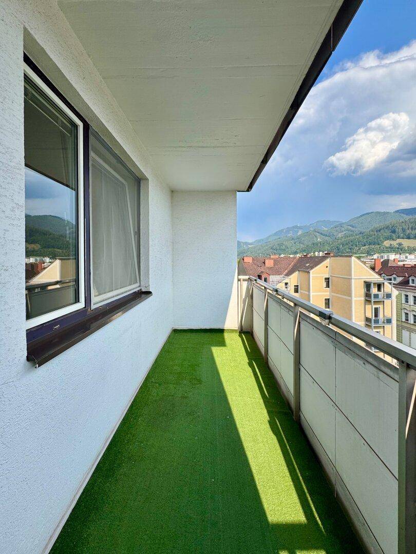 Balkon mit Kunstrasen und einem weiten Blick über die Stadt und die umliegenden Berge.