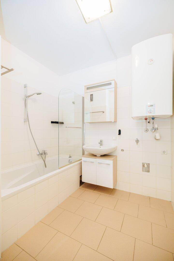 Badezimmer mit Badewanne, Duschabtrennung, Waschbecken und einem Warmwasserboiler.