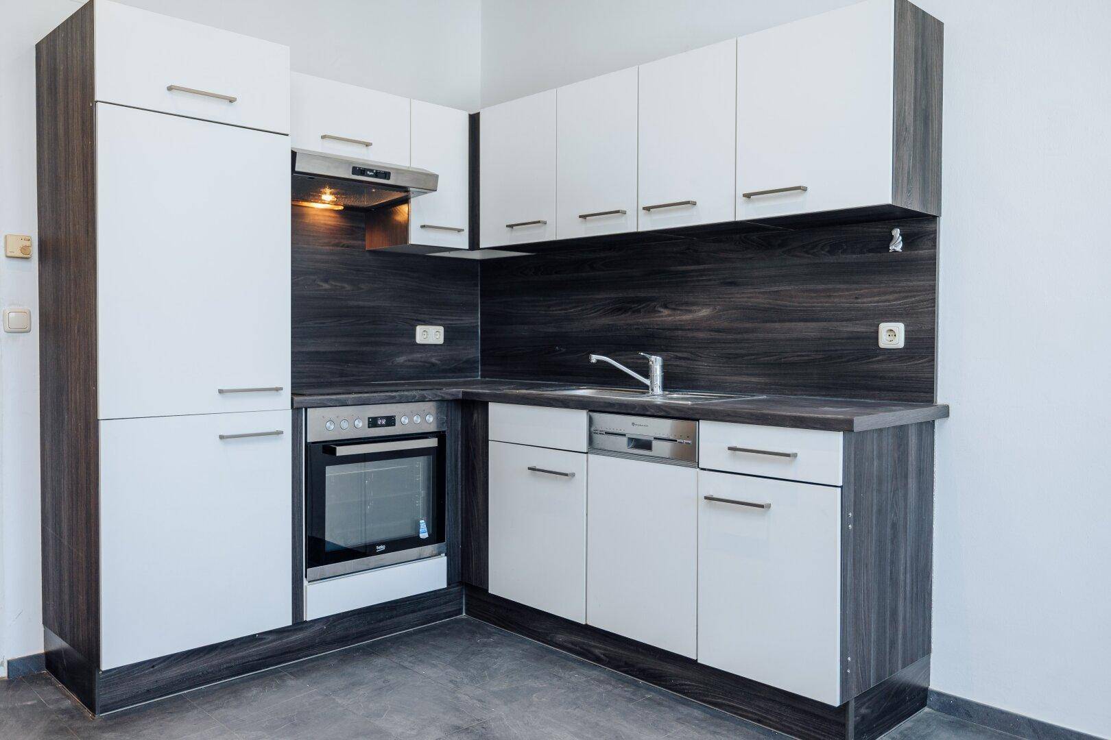 Moderne Einbauküche mit weißen Fronten, integriertem Backofen und Dunstabzugshaube.