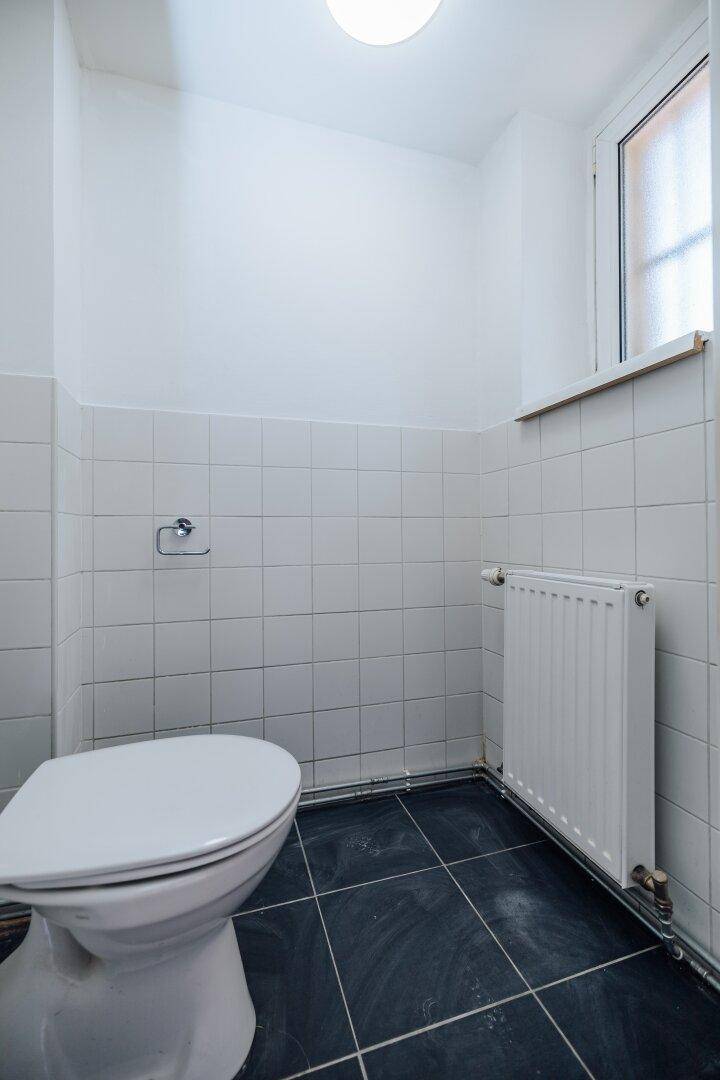 Separates WC mit Fenster, klassischer Toilette und dunklen Bodenfliesen, hell und sauber.