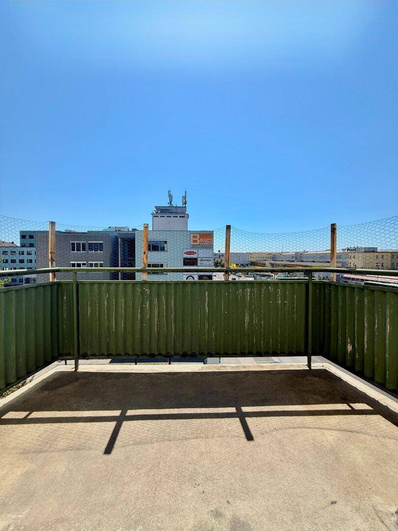 Balkon mit grüner Brüstung und Blick auf die umliegenden Stadtgebäude unter blauem Himmel.