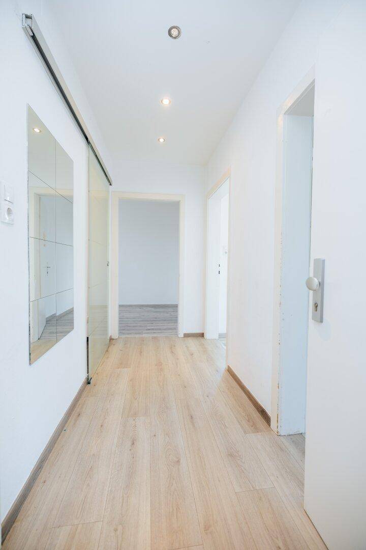 Heller Flur mit hellem Laminatboden, Einbaustrahlern und einer Spiegelschiebetür.