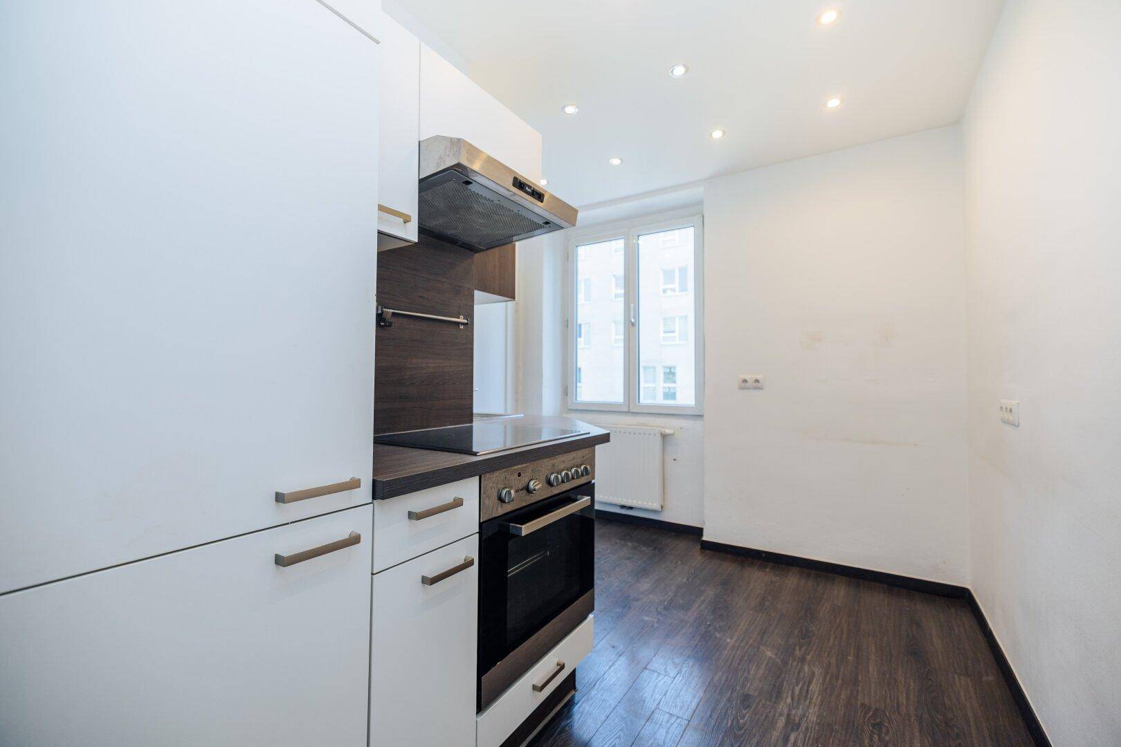 Moderne Küche mit weißen und dunklen Holzschränken, Backofen und Dunstabzugshaube.