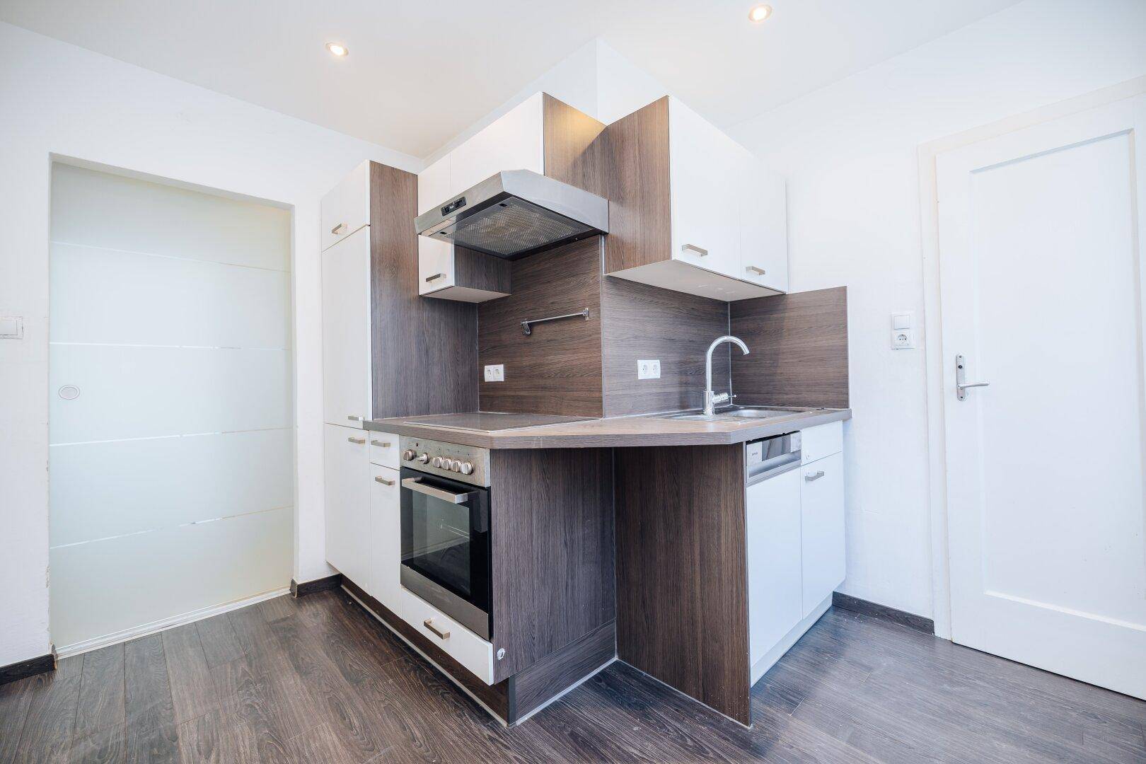 Funktionale Küche mit weißen und dunklen Holzschränken, Spüle, Backofen und Geschirrspüler.