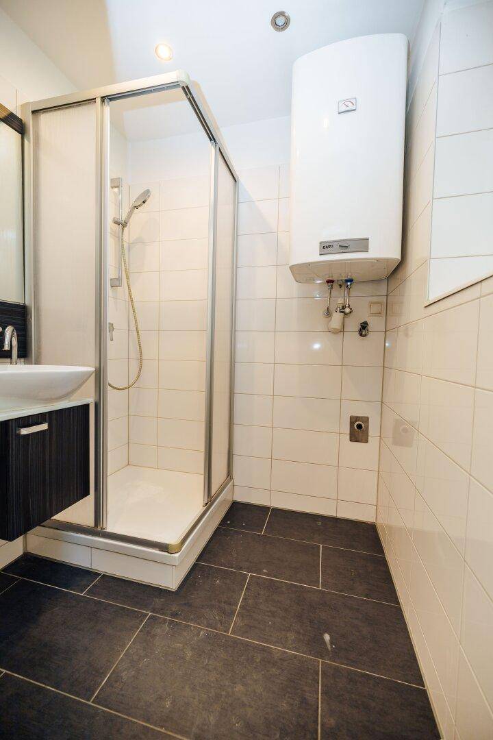 Badezimmer mit Duschkabine, Waschbecken und einem Warmwasserboiler an der Wand.