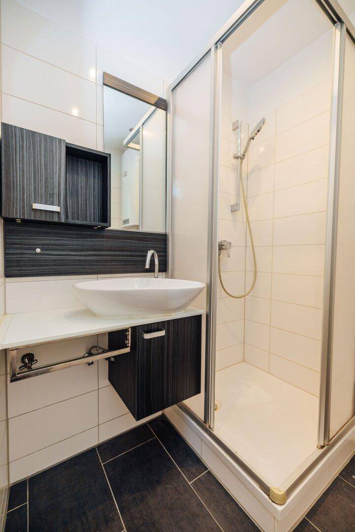 Modernes Badezimmer mit Duschkabine, elegantem Waschbecken und dunklen Holzschränken.