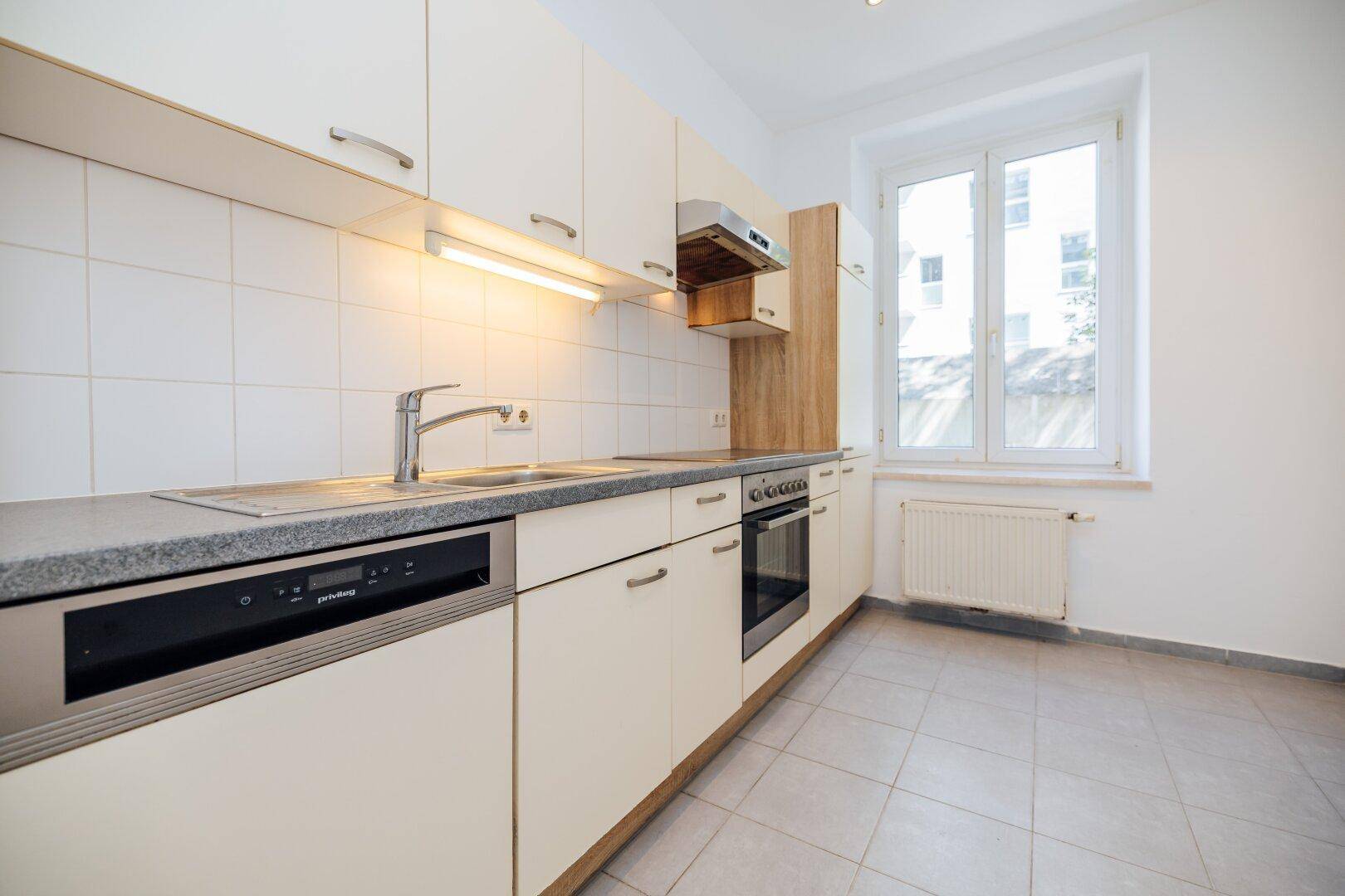 Funktionale Küche mit hellen Einbauschränken, Spülmaschine und Fenster, bereit zur Nutzung.