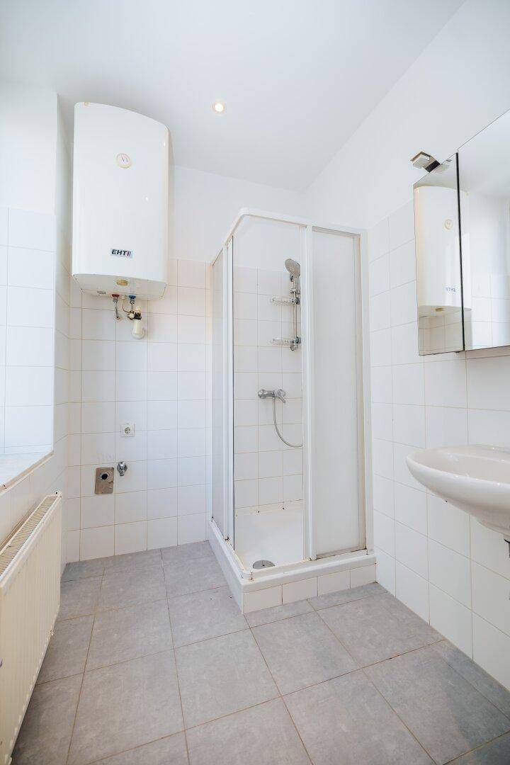 Funktionales Badezimmer mit Duschkabine, Waschbecken und Boiler, hell gefliest.