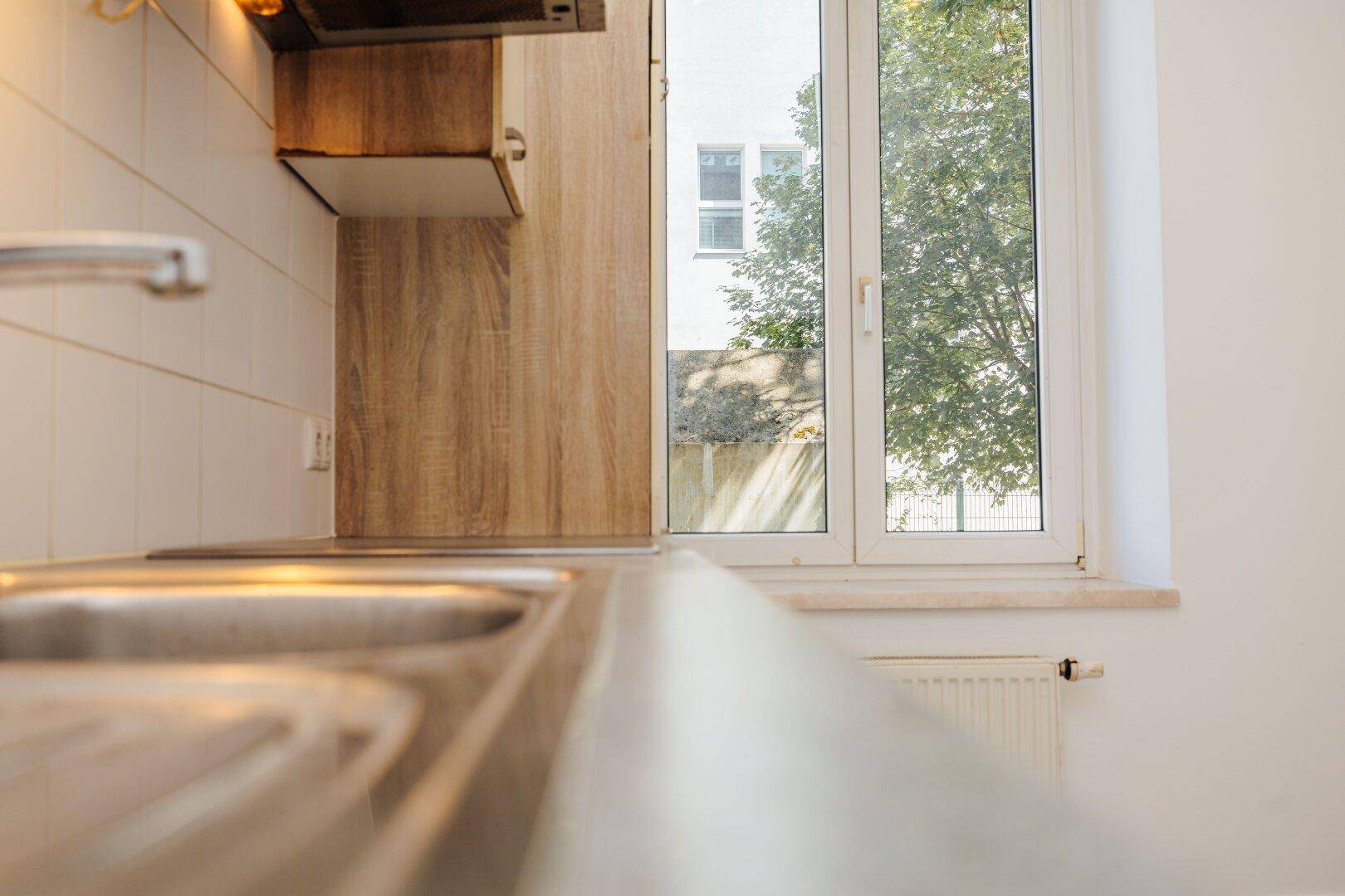 Detailansicht der Küchenspüle mit Blick aus dem Fenster auf Bäume und Gebäude.