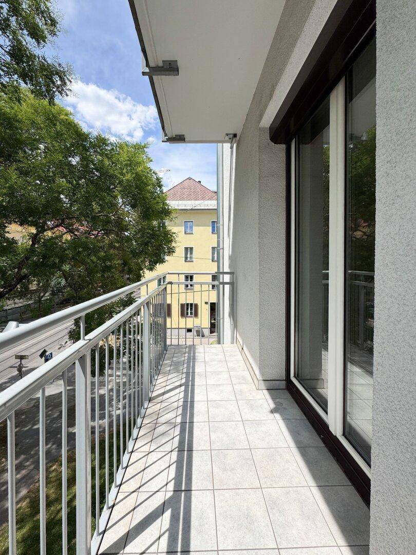 Heller Balkon mit Fliesenboden, Rollläden und Blick auf die umliegenden Gebäude.