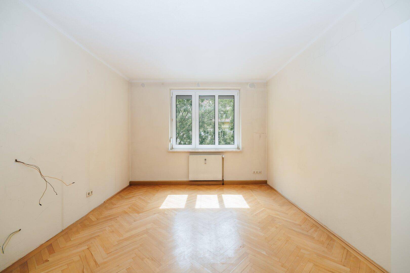 Helles Zimmer mit Fischgrätparkett und großem Fenster, ideal als Schlaf- oder Arbeitszimmer.