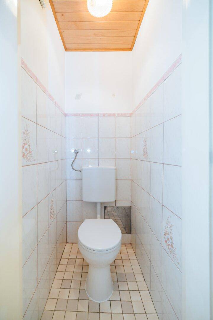 Separates WC mit Toilette und hellen Fliesen an Wänden und Holzdecke.