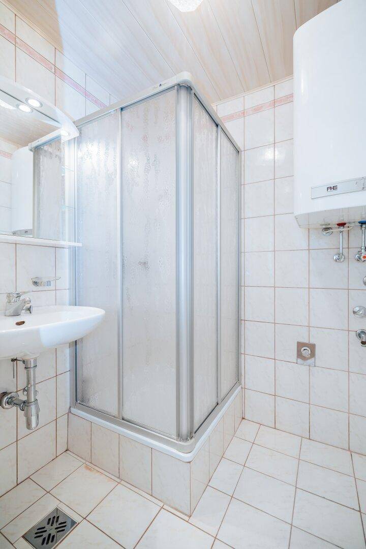 Kleines Badezimmer mit Duschkabine, Waschbecken und hellen Fliesen an Wänden und Boden.