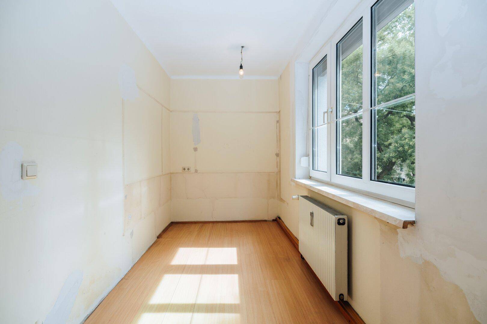Sonniger Raum mit Holzboden, großem Fenster und Heizkörper, ideal als Schlafzimmer.