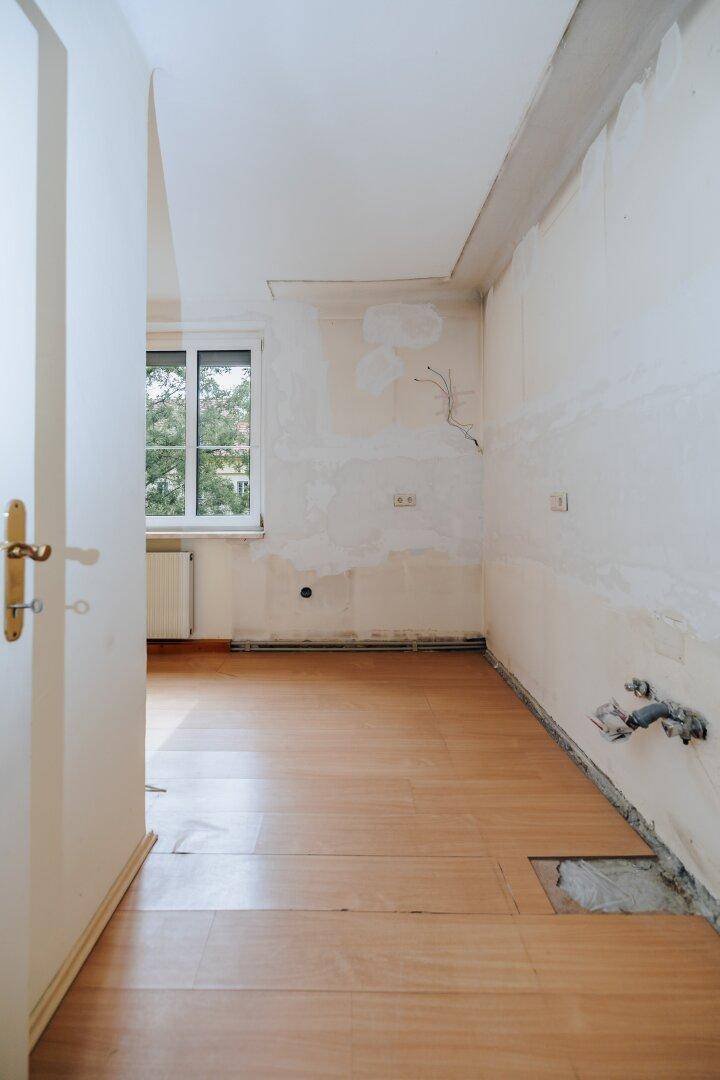 Raum mit Holzboden und Fenster, vorbereitet für die Installation einer neuen Küche.