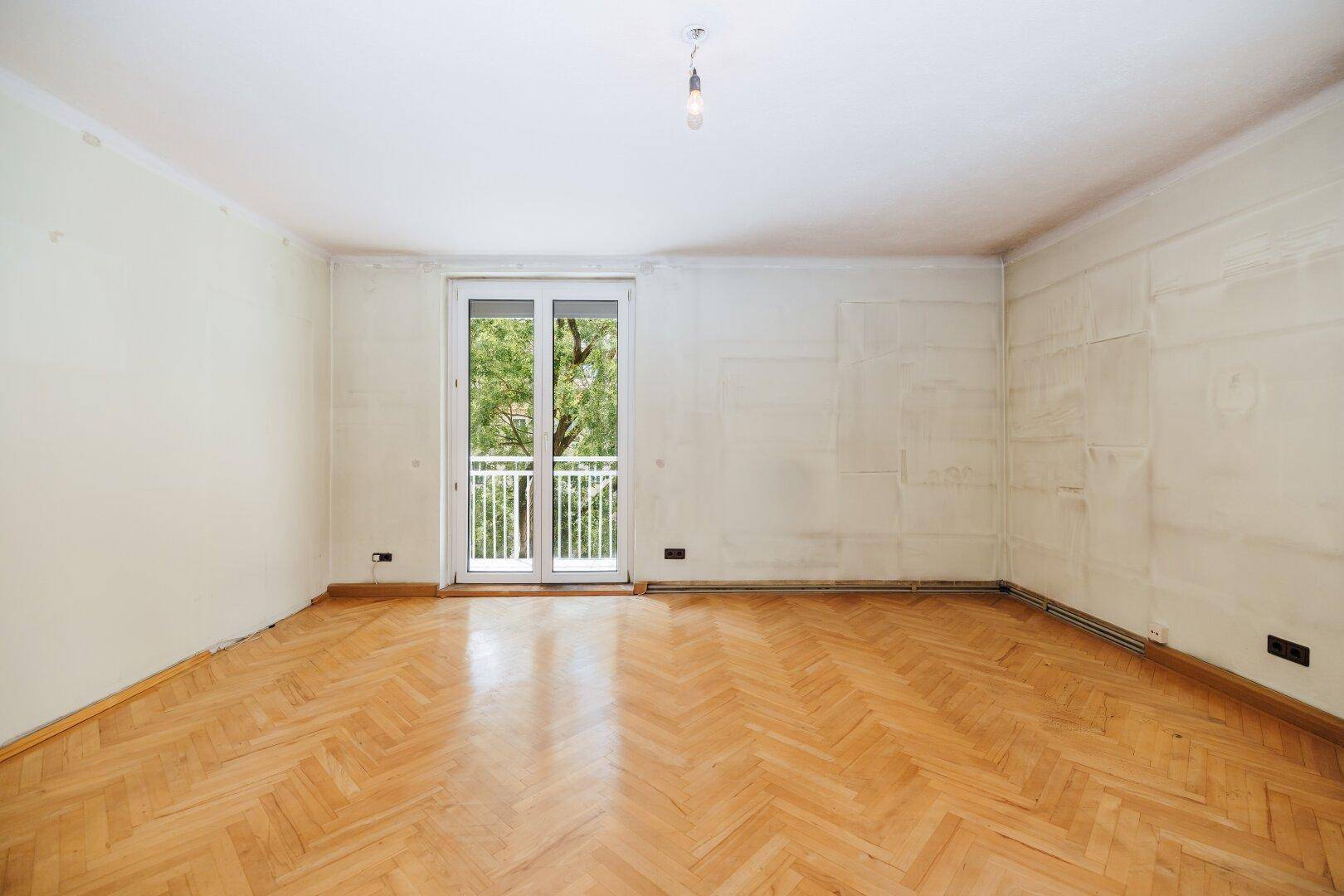 Helles Wohnzimmer mit Fischgrätparkett und Balkontür, bereit für eine Modernisierung.