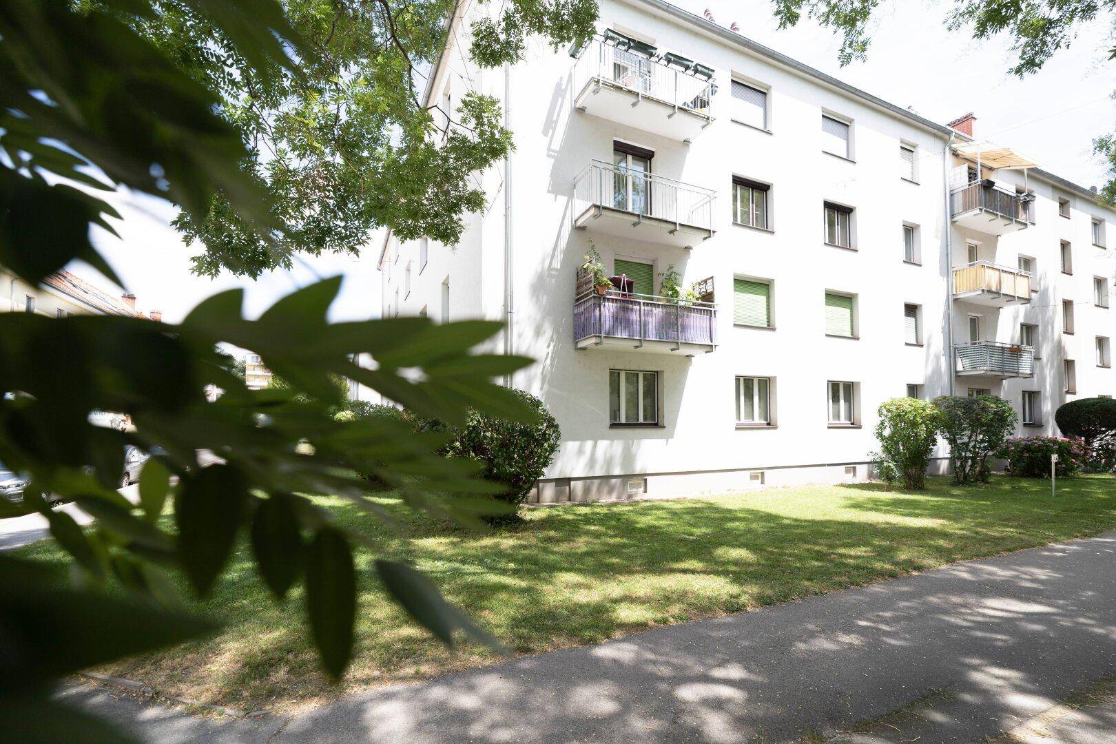 Weißes Mehrfamilienhaus mit mehreren Balkonen und einer gepflegten Rasenfläche im Vordergrund.