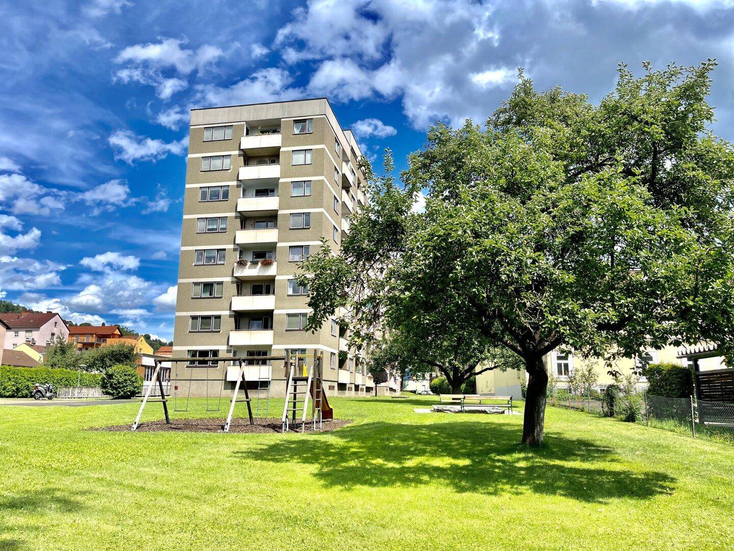 Mehrstöckiges Wohngebäude mit großem Gemeinschaftsgarten und Kinderspielplatz.