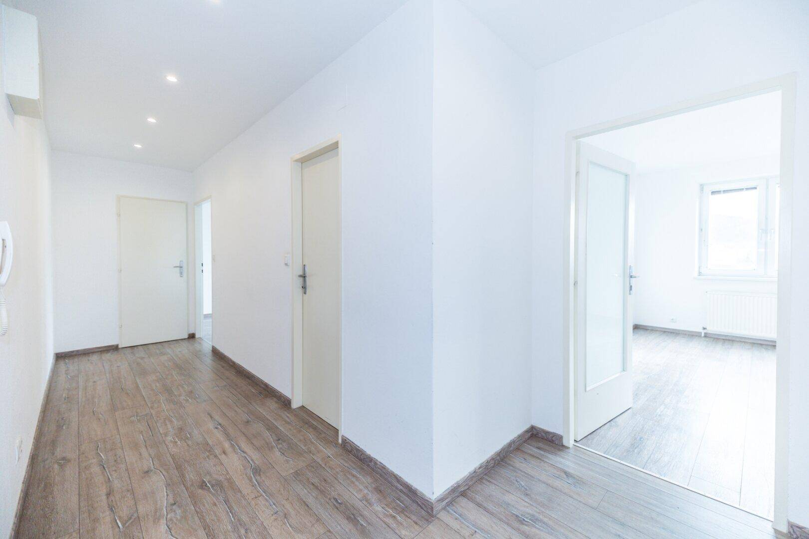 Heller Flur mit Laminatboden, weißen Wänden und modernen Deckenspots.