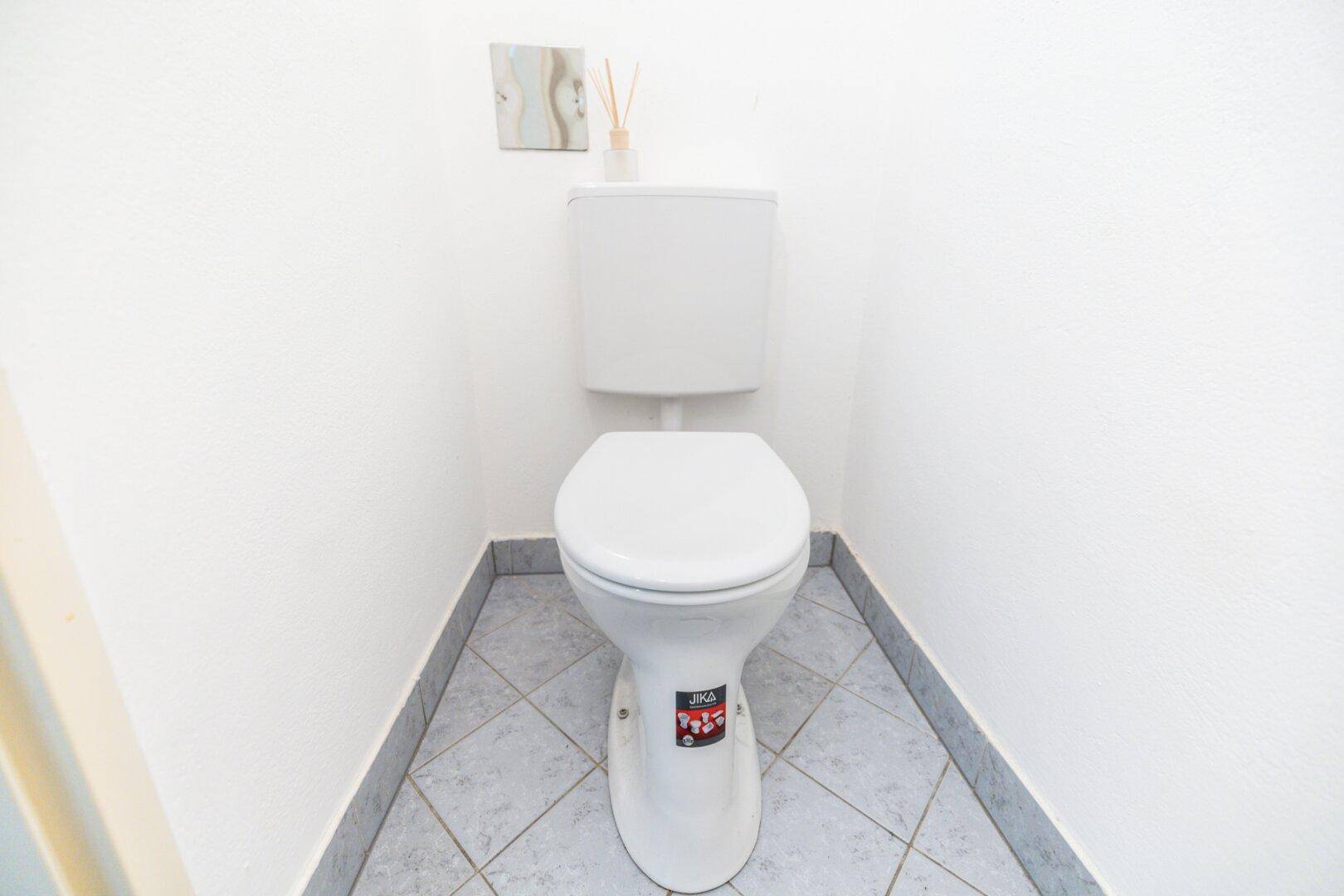 Separates WC mit Toilette und gefliestem Boden in schlichtem Design.