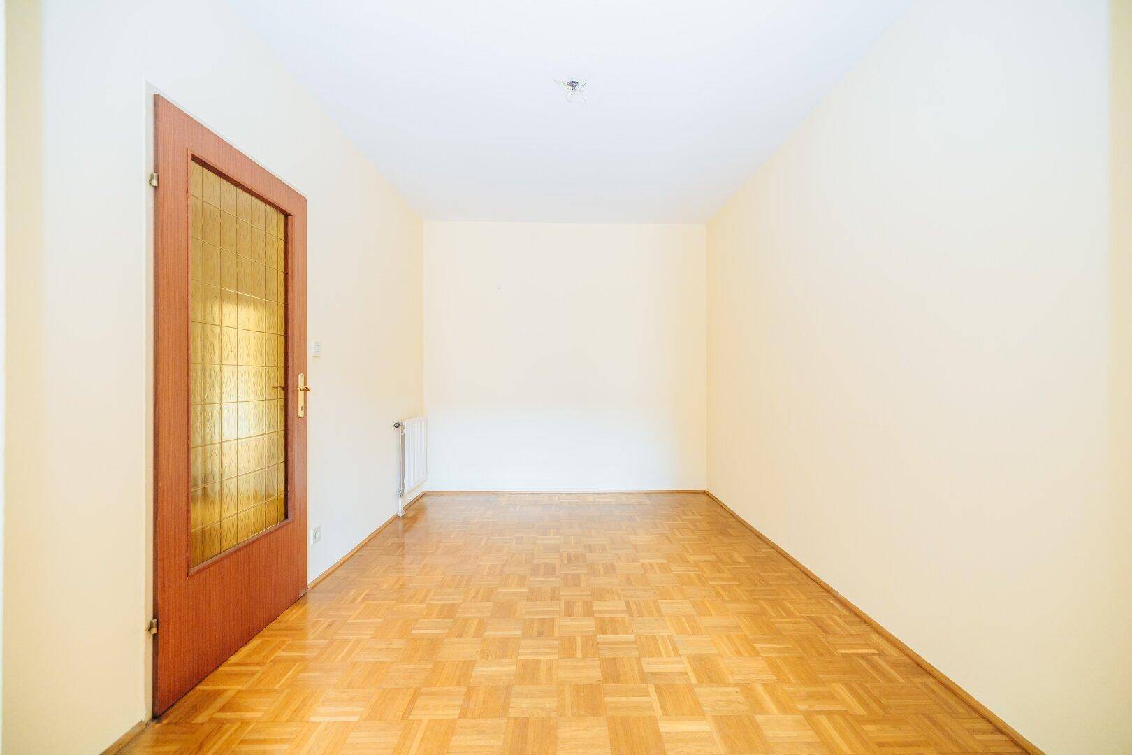 Helles Zimmer mit Parkettboden und einer Tür mit Glaseinsatz, ideal als Wohn- oder Essbereich.