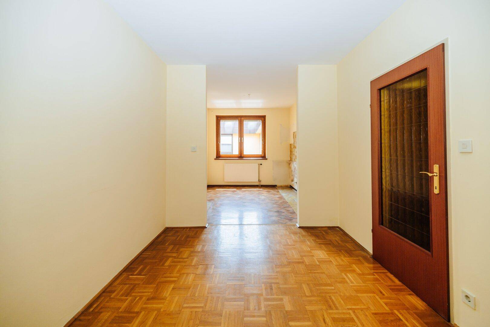 Offener Übergang von einem Zimmer mit Parkettboden in einen weiteren Raum mit Fenster.