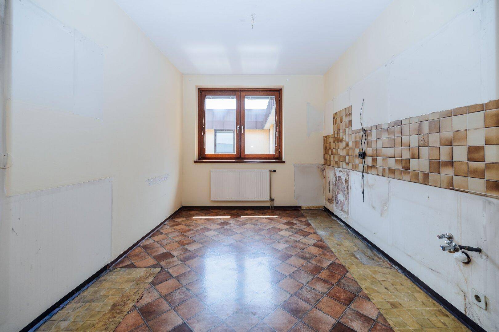Leere Küche mit alten Fliesen und Fenster, bereit für eine komplette Renovierung.