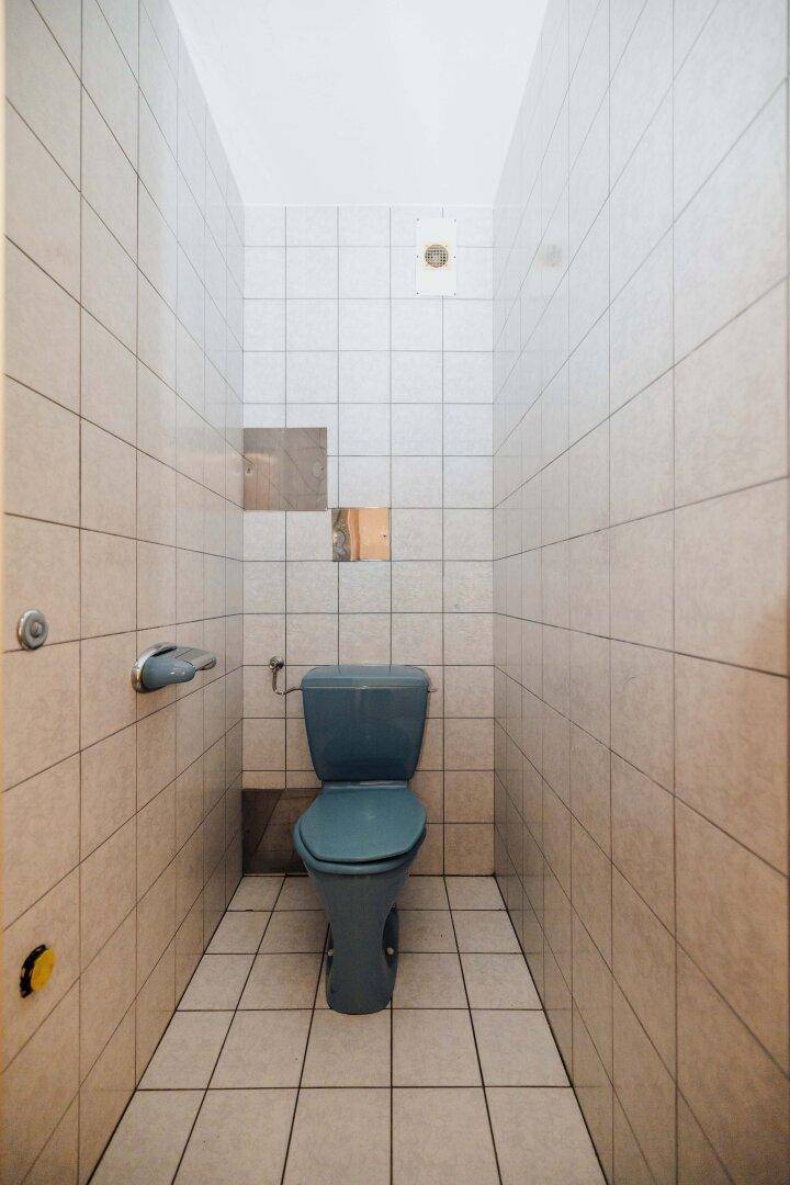 Separates WC mit hellen Fliesen und einer blauen Toilette, funktional und einfach gehalten.