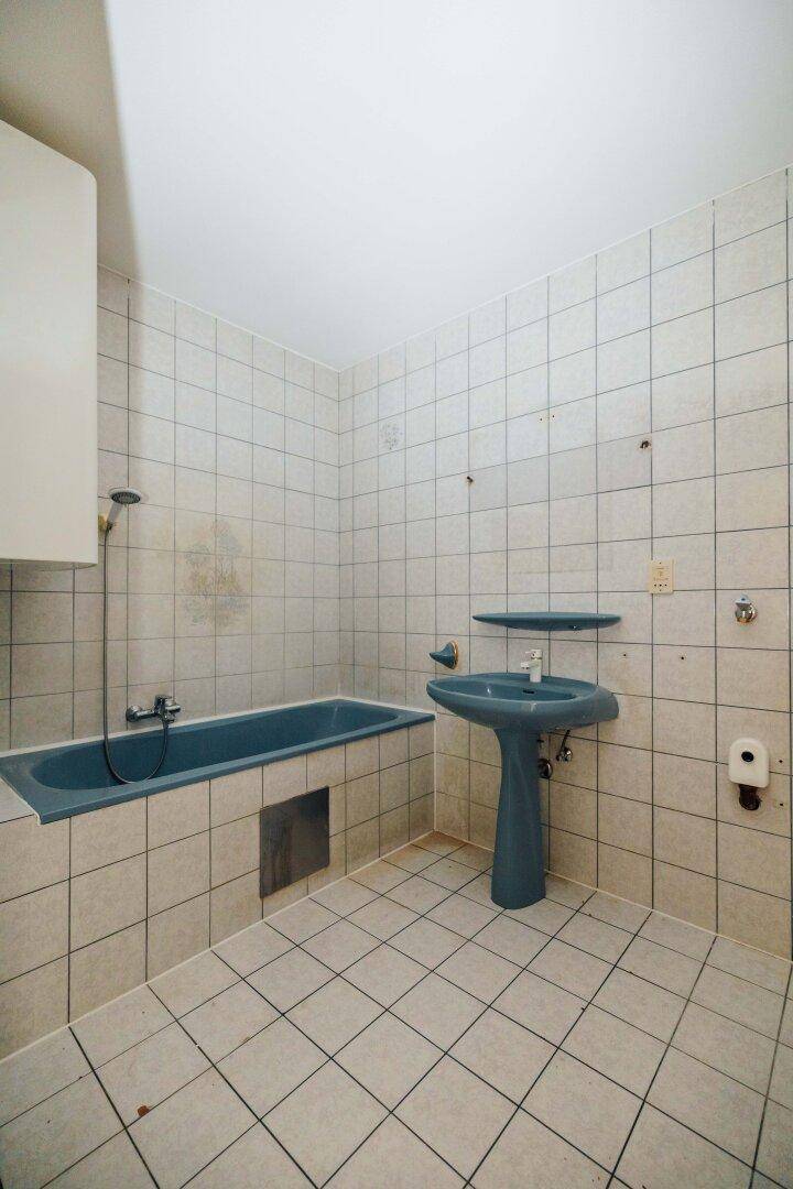 Badezimmer mit hellen Fliesen, einer blauen Badewanne und passendem Waschbecken im Stil der 80er Jahre.