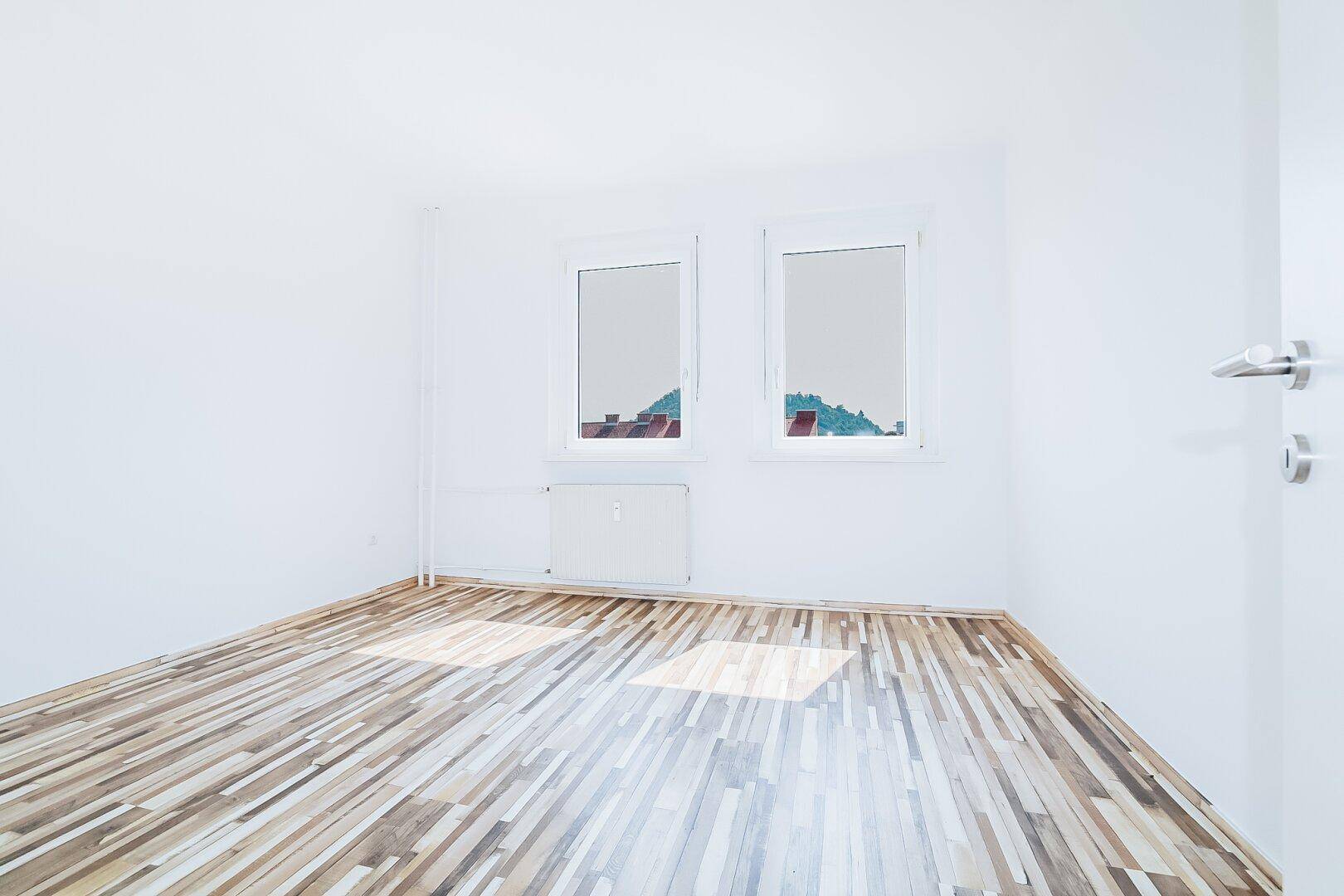 Helles, geräumiges Zimmer mit Laminatboden und zwei Fenstern, das viel Tageslicht bietet.
