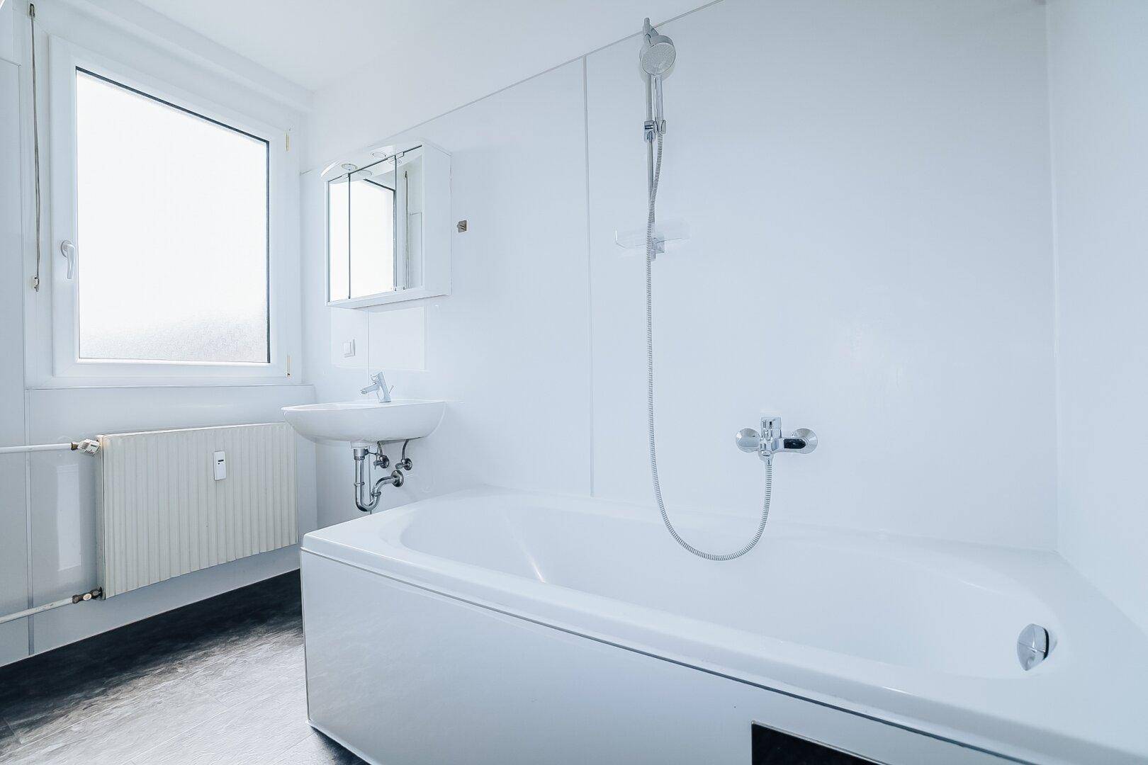 Helles Badezimmer mit Badewanne, Duschfunktion, Waschbecken und Spiegelschrank, inklusive Fenster.
