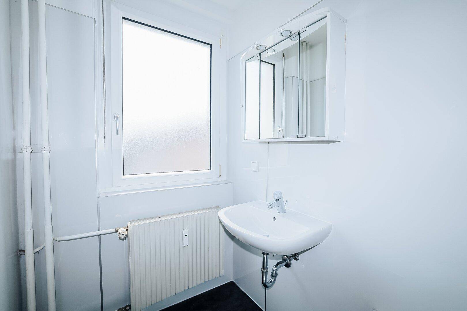Badezimmer mit Waschbecken, Spiegelschrank und Fenster, das für natürliche Belüftung sorgt.