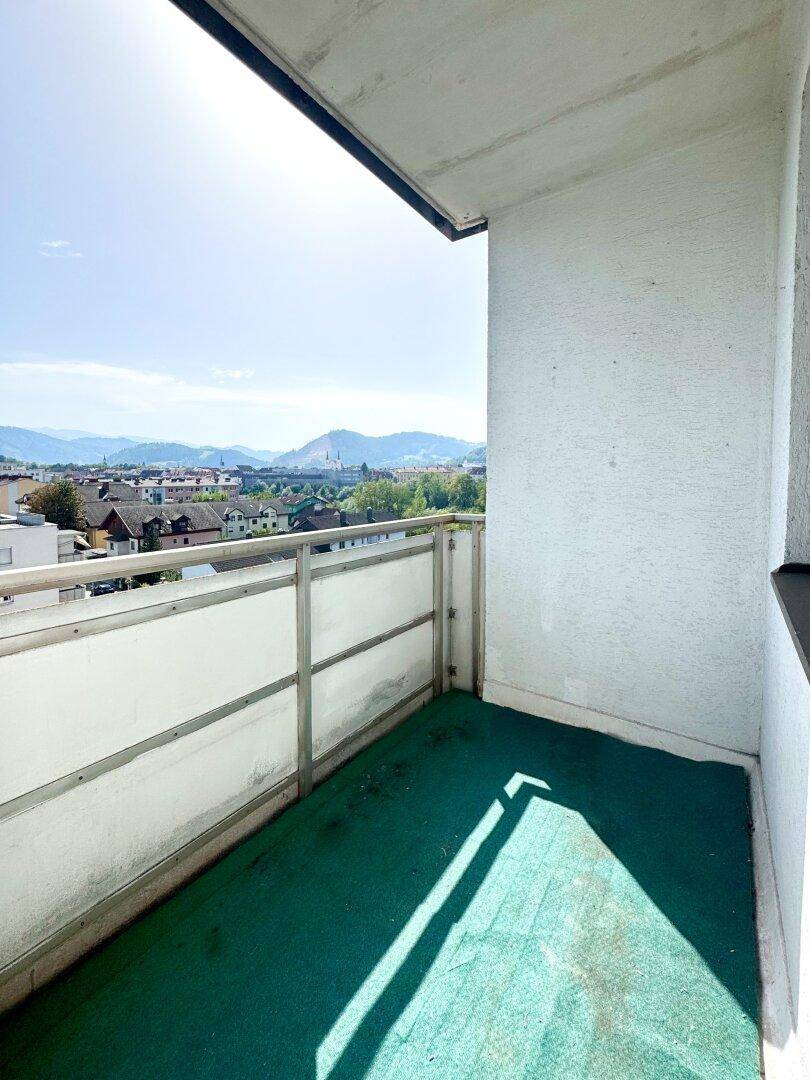 Balkon mit Metallgeländer und weitem Blick über die Stadt und die grüne Umgebung.