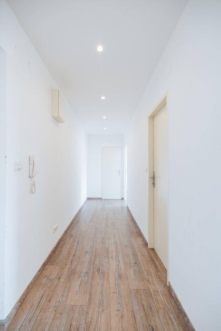 Langer, heller Flur mit Laminatboden und integrierter Deckenbeleuchtung.